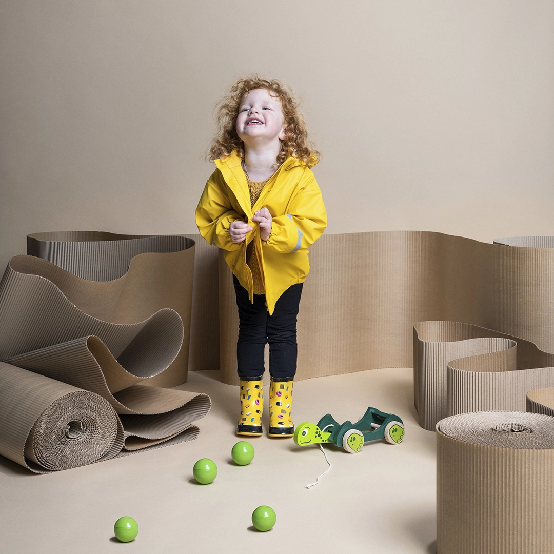 A child in yellow raincoat laughing their toys placed in front of them. Brand imagery for PMU by NyStudio