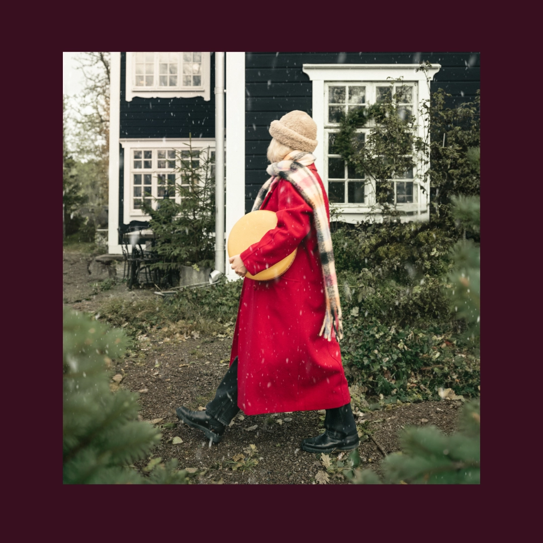 Woman in a red coat walking with a big cheese under her arm - Ny Studio